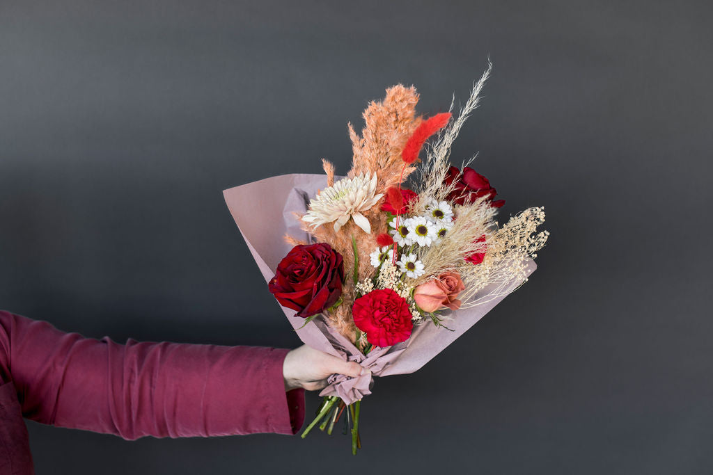 Hand held flower arrangement including vibrant red roses, carnations, and dried florals 